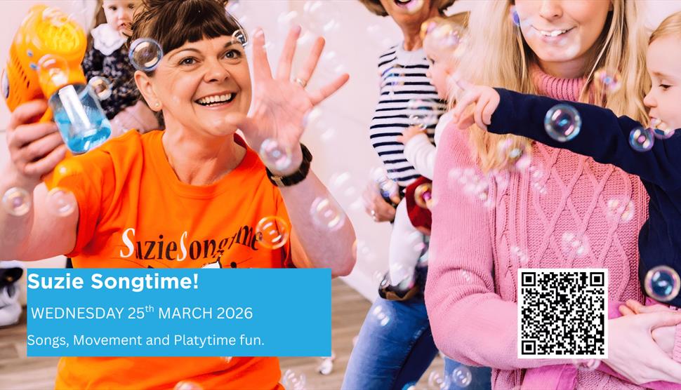 Parents holding babies innards dancing to music while Suzie the entertainer blows bubbles from a bubble machine around them