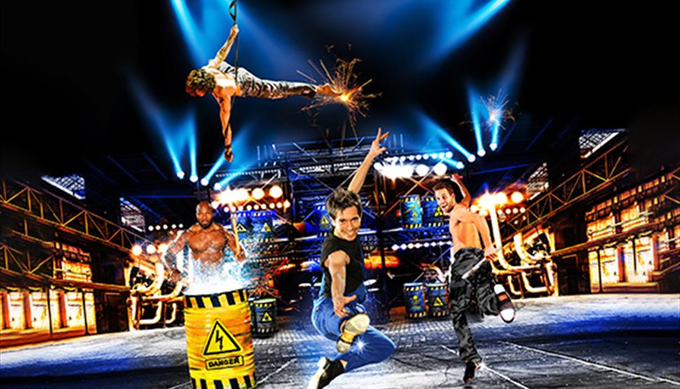 Two men dancing, one doing acrobatics, and another playing a drum with water coming off the top