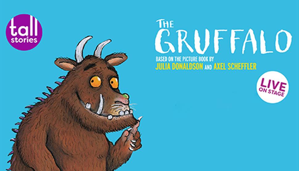 An illustration of The Gruffalo smiling. There is a purple circle with white text saying 'tall stories' in the top left corner, on the right is the 'T