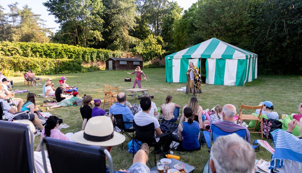 Ariel and prospero stand in a beautiful garden while the audience looks on
