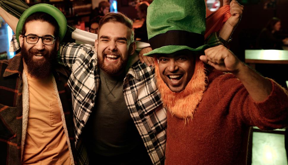 Three men celebrating with green hats, one has an orange beard.