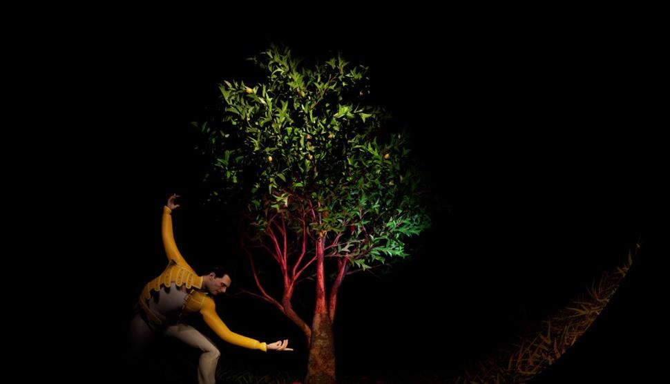 A performer in a yellow costume reaches towards a lit tree in a dance-like pose.