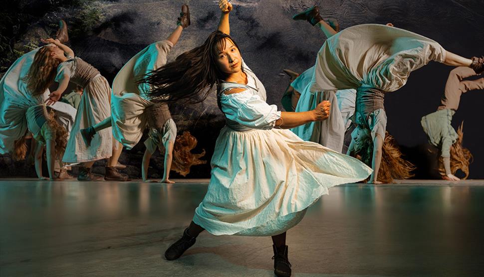 A woman in a white dress dances energetically, captured in mid-motion with multiple blurred images of her spinning in the background.