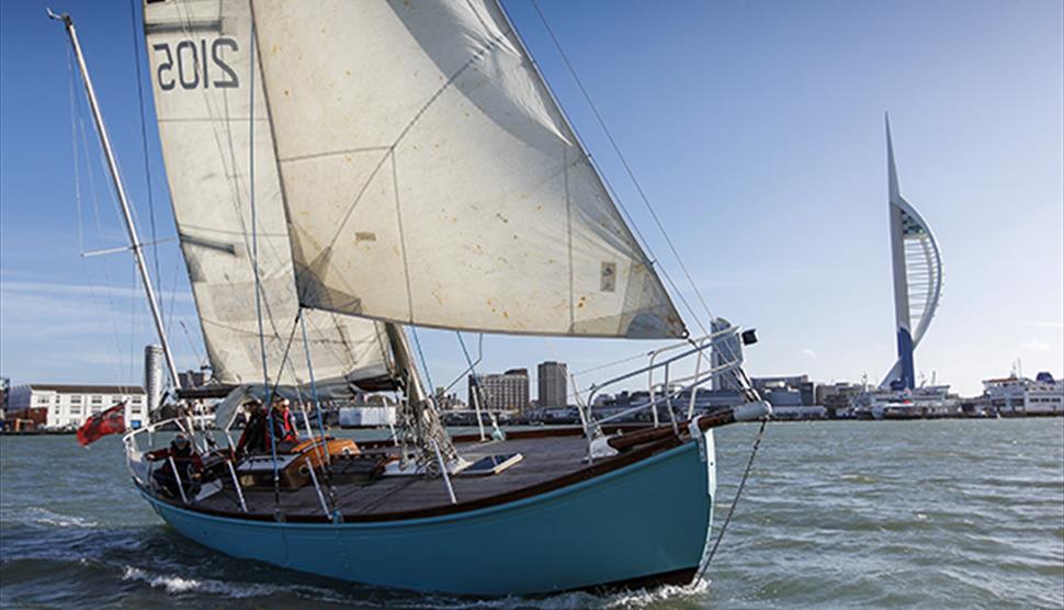 Historic yawl Lively Lady sailing on the Solent, a classic wooden vessel with tall masts and sails set against open water and coastline.
