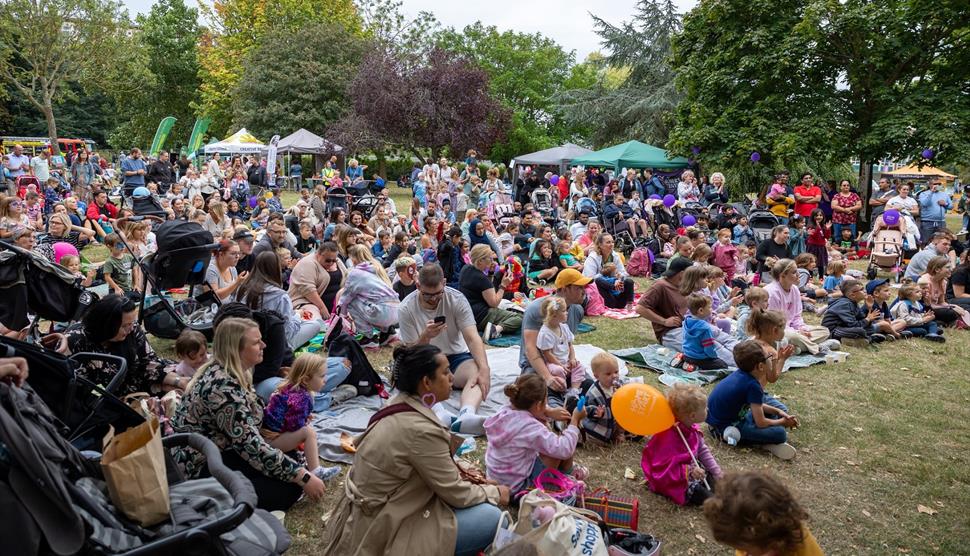 Lots of family groups sat on grass with gazebos in the background.