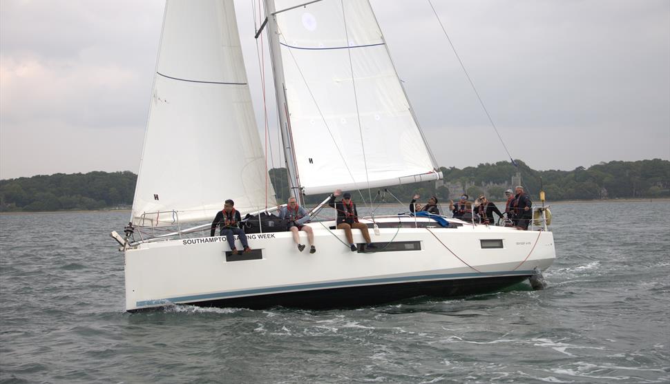 3 sailing boats on the water, with sailors sitting on the side waving at the camera