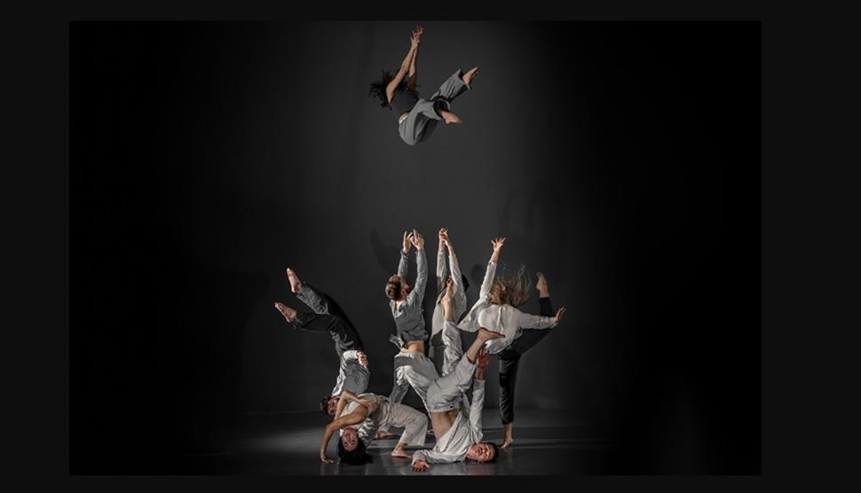 A group of dancers dressed in grey clothes one of the dancers has been thrown up.