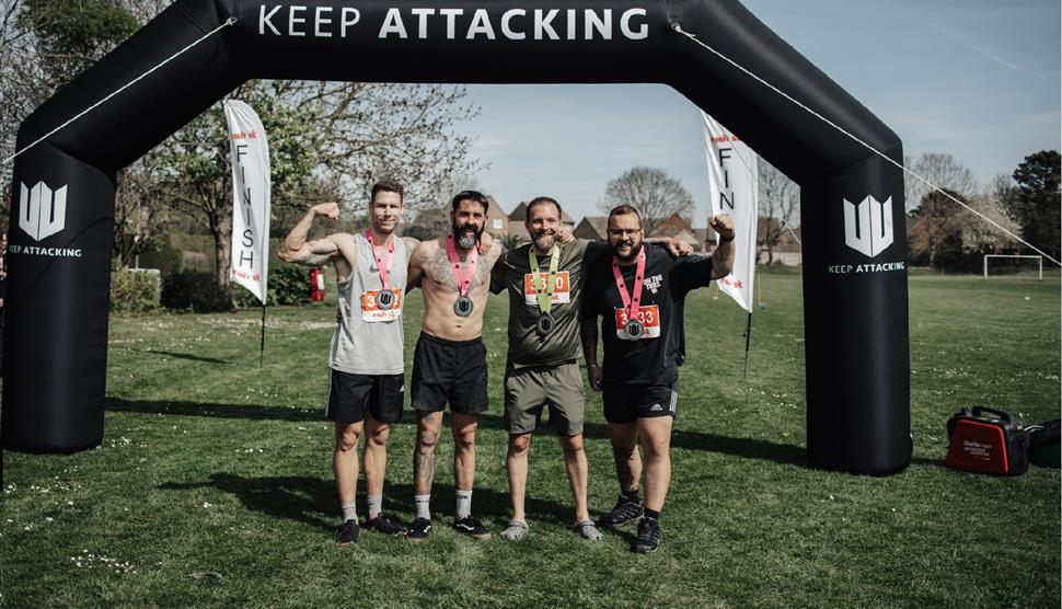 Four men with medals stood in front of an inflatable arch saying Keep Attacking.