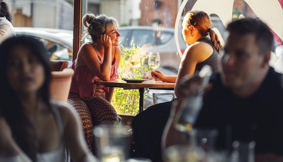 customers enjoying conversation over a glass of wine with dappled sunlight through the window