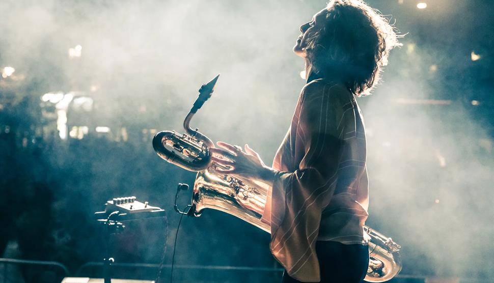 Tamar Osborn is facing away, holding her baritone saxophone with smoke in the background