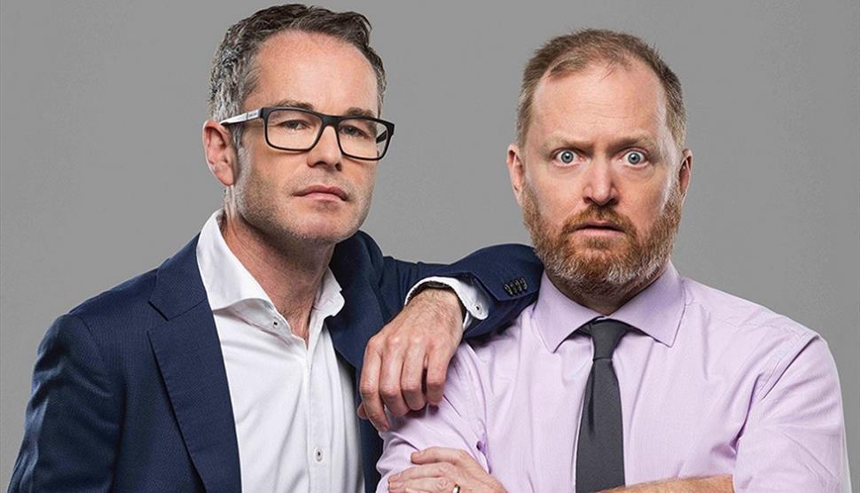 Two white men, one wearing glasses with a shirt and jacket. The other has a beard with a shirt and tie.