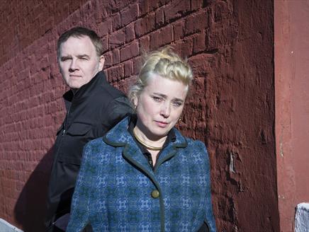 A man and a blonde woman stand together in front of a building.