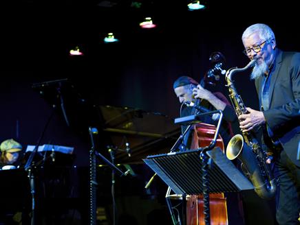 A saxophonist, double bassist and pianist perform on stage.