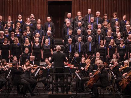 On the stage at the O2 Southampton, the choir stand on the choir steps as the orchestra perform on the stage, with the conductor standing in front of