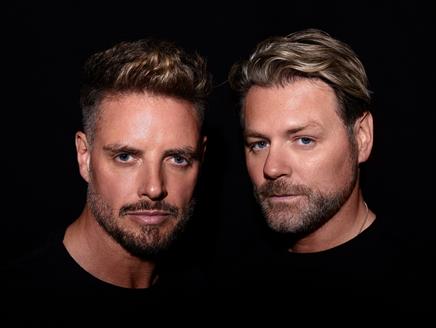 Keith Duffy and Brian McFadden in black tops with a black background looking at the camera