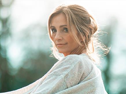 Cara Dillon wearing a neutral colour cardigan, standing what looks like outside, and smiling gently at the camera