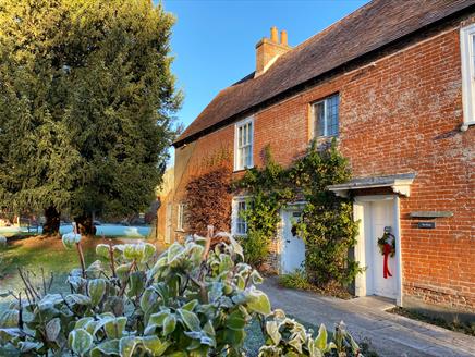 Jane Austen's House in winter.  Frost is on the ground and a red wreath decorates the door.