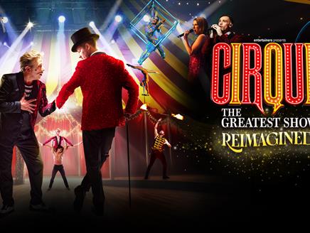 Two circus performers on stage shaking hands with various other circus acts happening behind them
