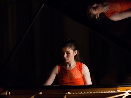 Cordelia Williams is sat at a piano looking downwards.