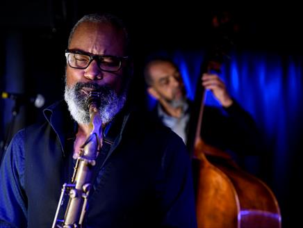 Denys Baptiste is in the front of the shot playing the tenor saxophone, and Gary Crosby OBE is playing acoustic bass behind him.