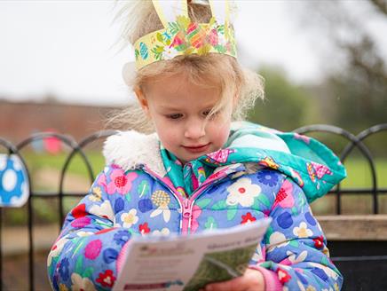 Child wearing bunny ears while looking at an Easter trail sheet.
