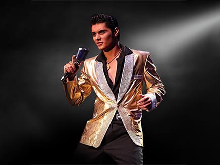 Emilio Santoro dressed as Elvis in a shiny gold suit jacket, holding a microphone on a dark background