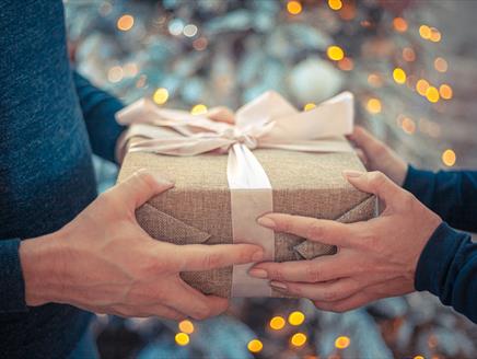 A wrapped gift is being passed from one pair of hands to another