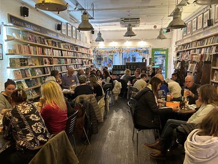 Groups of people sitting at tables in a bookshop with drinks taking part in a quiz