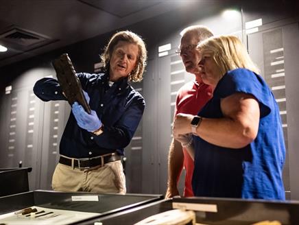 A member of the Mary Rose Museum team showing an artefact to a man and woman.