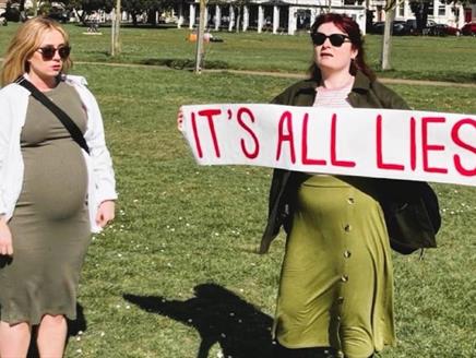 Two women on Southsea Common. One is pregnant, the other holds a white banner on which red text reads: It's all lies