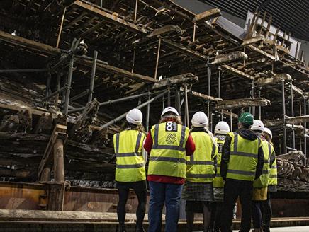 A group of people in high-vis jackets looking up at the salvaged hull of the Mary Rose.