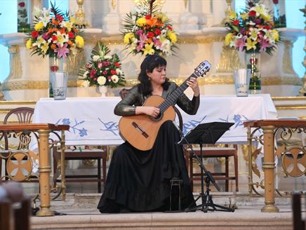 A woman with black hair plays the guitar in a cathedral.