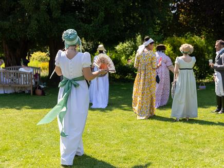 Visitors in Regency dress walking across the cottage garden at Jane Austen's House in summer