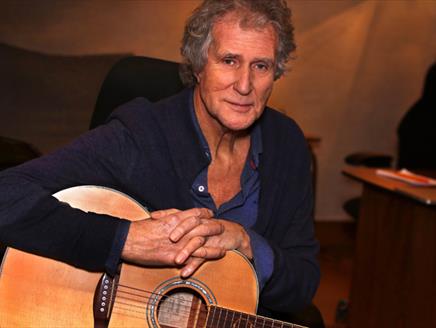 Photograph of John Illsley holding an acoustic guitar