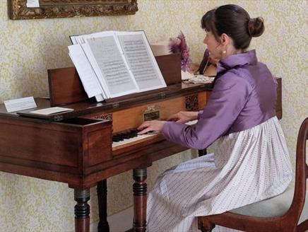 A woman in regency clothing playing on a piano