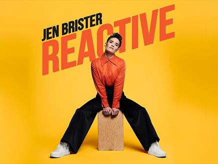 Comedian Jen Brister sat on a wooden box.