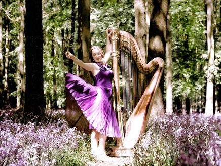 Keziah Thomas playing her harp in a beautiful, flowering spring wood.