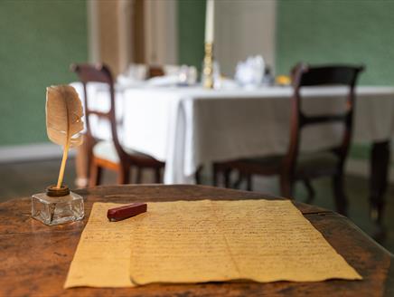 Jane Austen's small wooden writing table. A quill and letter sit on the table.