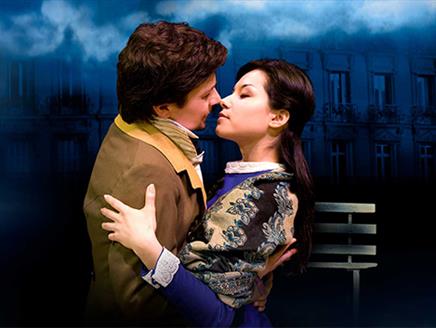 A romantic scene between two people dressed in period clothing. They are in an intimate embrace, about to kiss, with the man holding the woman tenderl