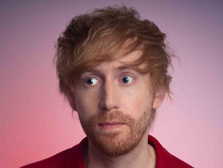 A close up of Mark Simmons wearing a shirt. He has a stubbly ginger beard and hair and wide, bright blue eyes
