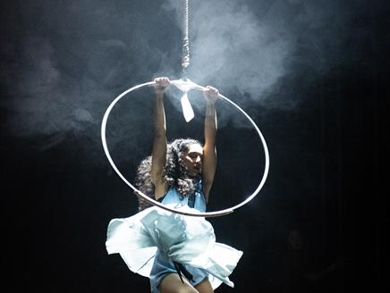 A circus performer dressed in a white dress hangs from an ariel hoop