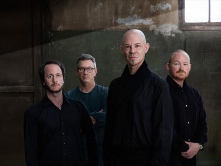 Four men stand in a room together.