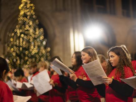 A group of children wearing red shirts sing from sheet music during a Gabrieli Roar concert performance in 2022. They stand in a warmly lit cathedral,