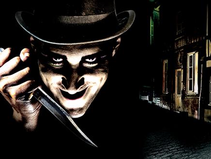 A very dark image with a Victorian era street in the background. The foreground is a man brightly lit from underneath, wearing a top hat and a knife l