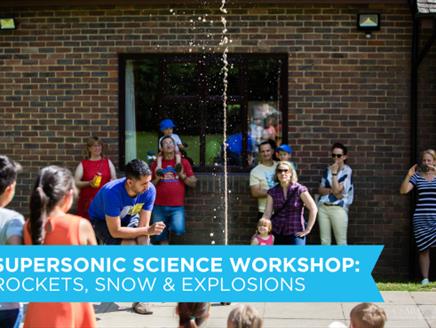 Children watching with awe at a science workshop demonstration of Mentos and Fizzy drinks explosion effect, outdoors.
