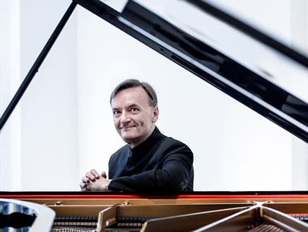 A man sits at a piano and looks towards the camera.