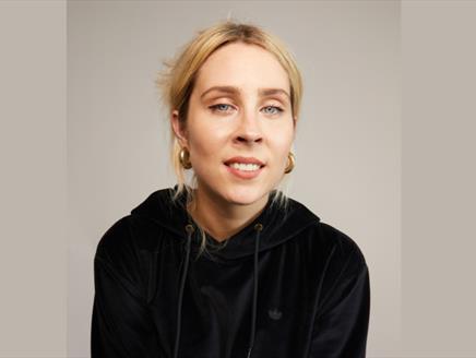 Poster image for Stevie Martin: Clout, showing the comedian in a black hoodie and stood against a brown background