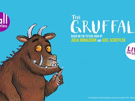 An illustration of The Gruffalo smiling. There is a purple circle with white text saying 'tall stories' in the top left corner, on the right is the 'T