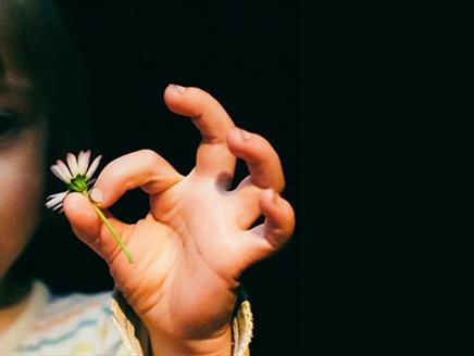 A young girl in a striped top holding a daisy on a dark background