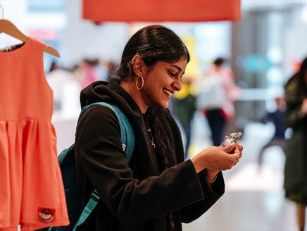 a young person with long dark hair watching a paper boat origami in their hand while attending an exhibition.